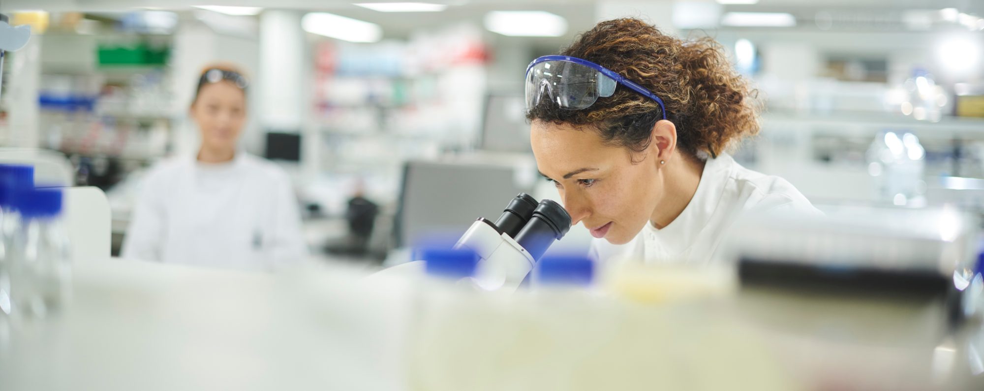 people in lab with woman in the foreground looking through microscope