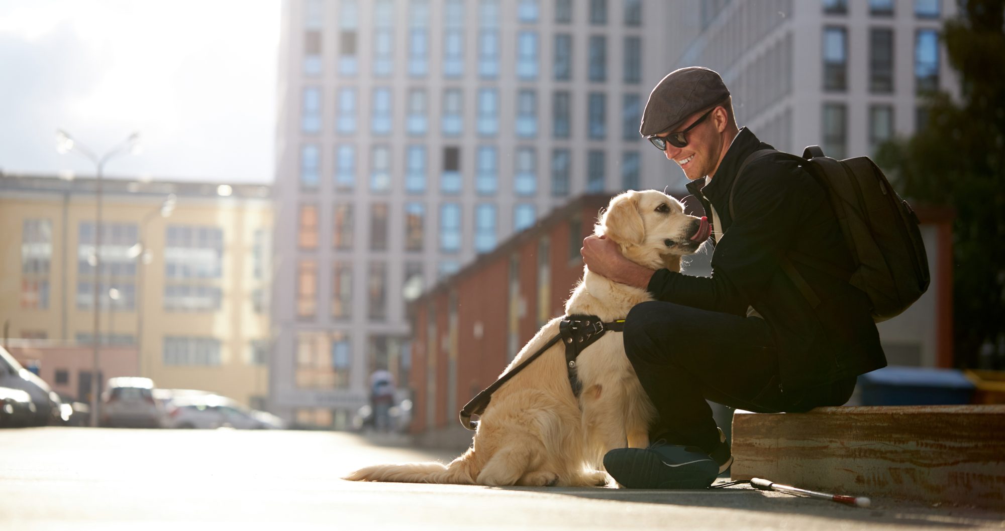 Blind man sitting on bench in public, petting his golden retriever